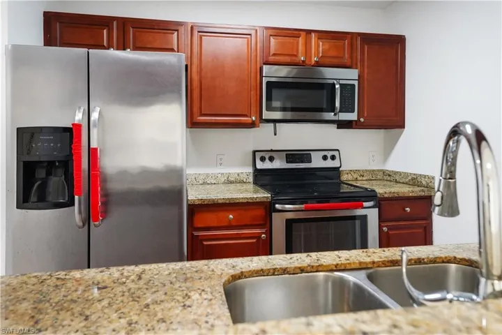 Kitchen featuring a double basin stainless steel sink with a high-arch faucet, granite countertops, wood-finish cabinetry, a stainless steel side-by-side refrigerator, and a stainless steel oven with an above-range microwave