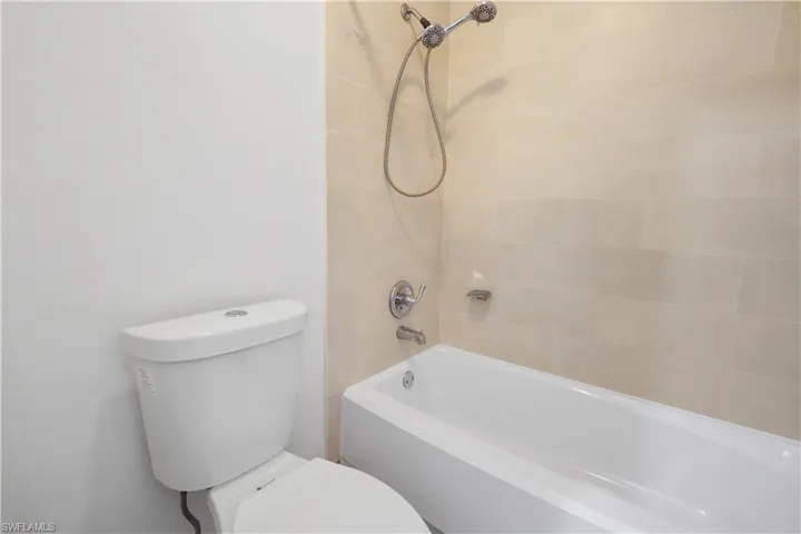 White tub and shower combination with light-toned tiled surround, chrome fixtures, and a handheld showerhead