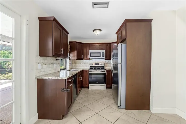 Kitchen with stainless steel appliances, sink, light tile patterned floors, decorative backsplash, and light stone countertops