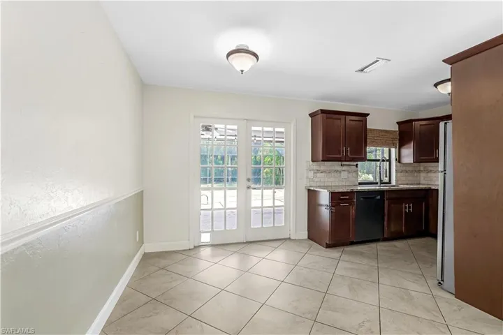 Kitchen with black dishwasher, white refrigerator, light stone counters, light tile patterned floors, and decorative backsplash