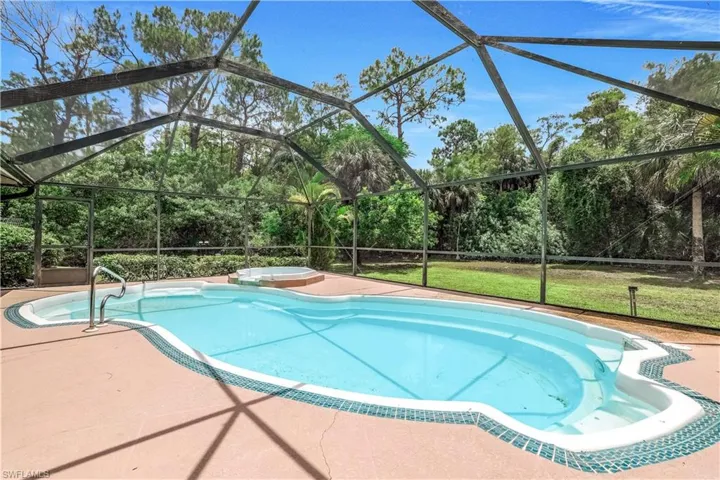 View of swimming pool featuring a patio, glass enclosure, and a hot tub