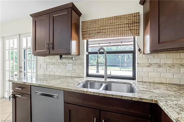 Kitchen with backsplash, light stone countertops, and dark brown cabinets
