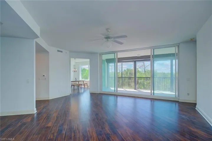 Unfurnished living room with dark wood-style flooring, floor to ceiling windows, ceiling fan, and a chandelier