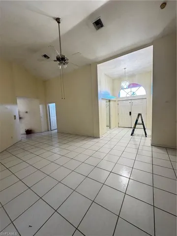 Spare room featuring ceiling fan, light tile patterned floors, a chandelier, and lofted ceiling