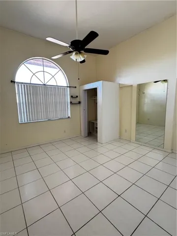Unfurnished bedroom featuring a high ceiling, light tile patterned floors, a ceiling fan, and a walk in closet