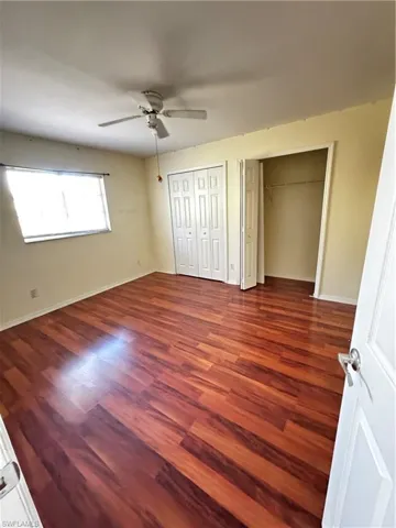 Unfurnished bedroom with multiple closets, dark wood-style floors, and a ceiling fan