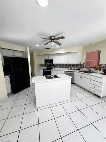 Kitchen featuring stainless steel appliances, light countertops, a center island with sink, white cabinets, and light tile patterned floors