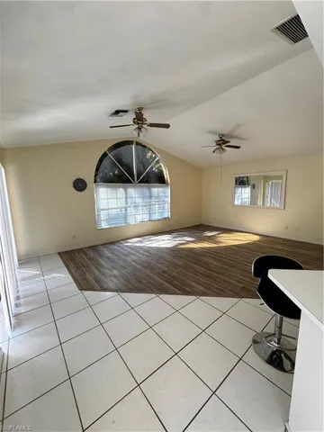 Unfurnished living room with light tile patterned floors, vaulted ceiling, and a ceiling fan