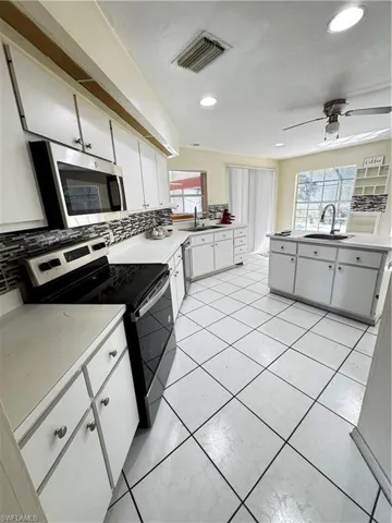 Kitchen with white cabinets, stainless steel range, decorative backsplash, light countertops, and recessed lighting