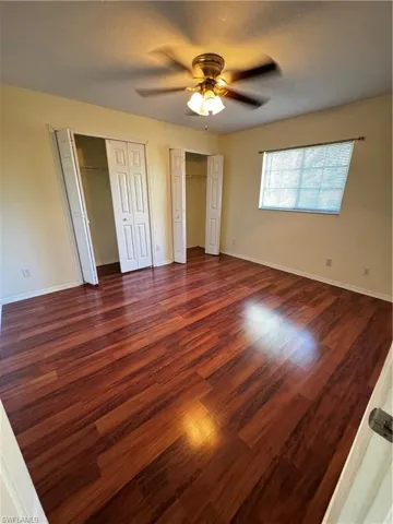 Unfurnished bedroom featuring two closets, dark wood-style floors, and ceiling fan