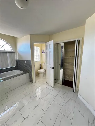 Full bathroom featuring a garden tub, light marble finish floors, and plenty of natural light