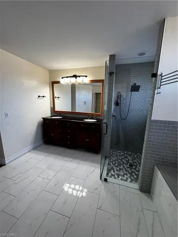 Bathroom featuring double vanity, light marble finish floors, and a stall shower