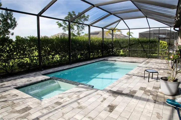 View of pool with a pool with connected hot tub, glass enclosure, a sunroom, and a patio area
