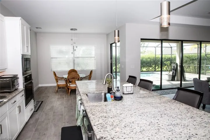 Kitchen with light stone counters, hanging light fixtures, white cabinets, stainless steel appliances, and a kitchen bar