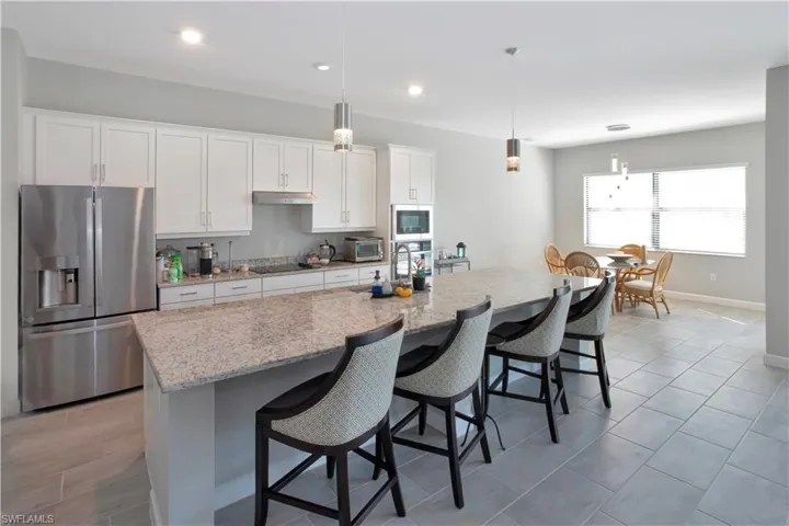Kitchen featuring appliances with stainless steel finishes, white cabinets, decorative light fixtures, light stone counters, and a kitchen breakfast bar