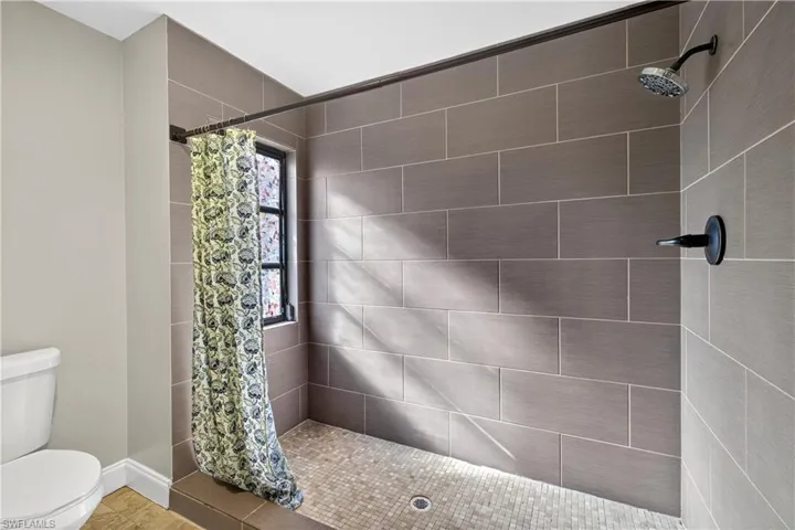 Shower stall featuring rectangular gray wall tiles, mosaic tile flooring, a window, and a matte black shower head and fixture