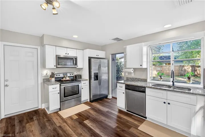 Modern kitchen featuring white cabinetry, granite countertops, stainless steel appliances, wood-finish flooring, and a large window above the sink