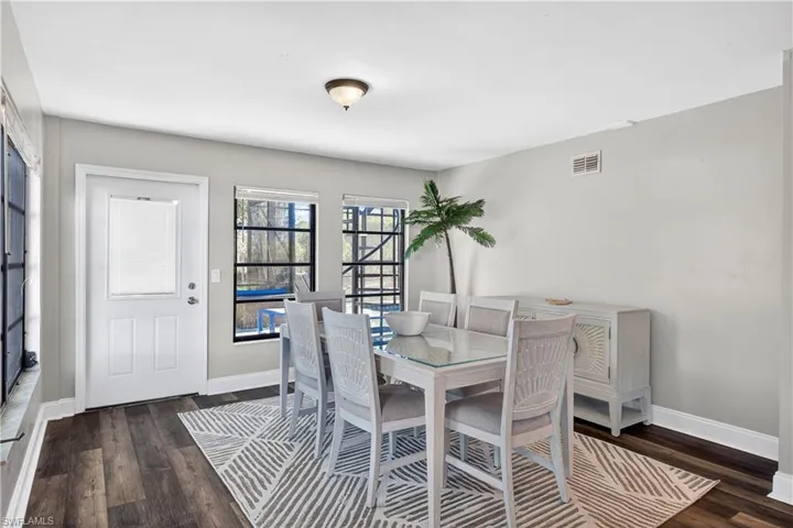Dining area featuring wood-finish flooring, light gray wall paint, a white paneled door with an integrated blind, and multiple windows with black framing