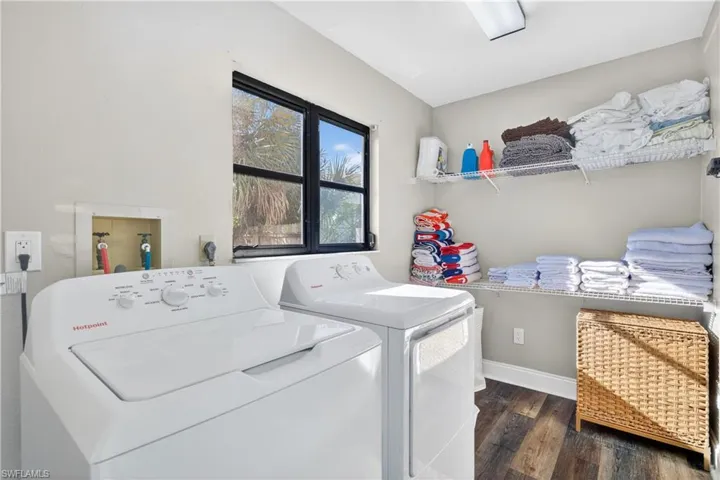 Dedicated laundry room featuring a washer and dryer, wood-finish flooring, a window with exterior visibility, overhead lighting, and built-in wire shelving