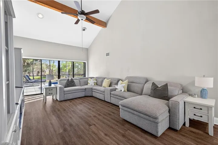 Spacious living area featuring wood-finish flooring, a soaring vaulted ceiling with an exposed wood beam, and a ceiling fan