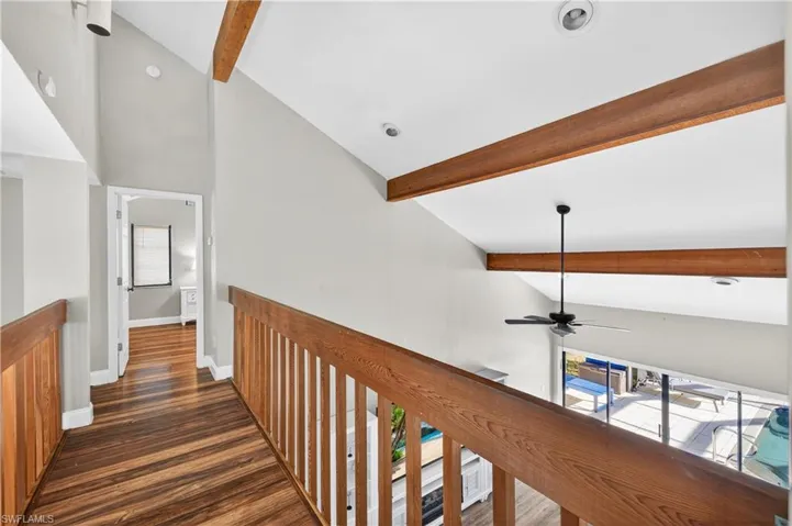 Upper-level hallway featuring wood-finish flooring, wood railings, vaulted ceilings with exposed wood beams, and recessed lighting