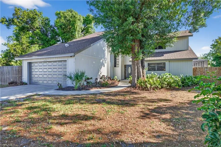 Contemporary-style home featuring a two-car garage with a paneled door, a paved driveway, a walkway to the front entrance, a dark front door with decorative glass, and established landscaping