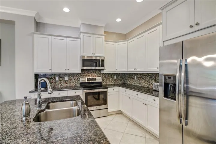 Kitchen with dark stone counters, stainless steel appliances, white cabinets, and sink