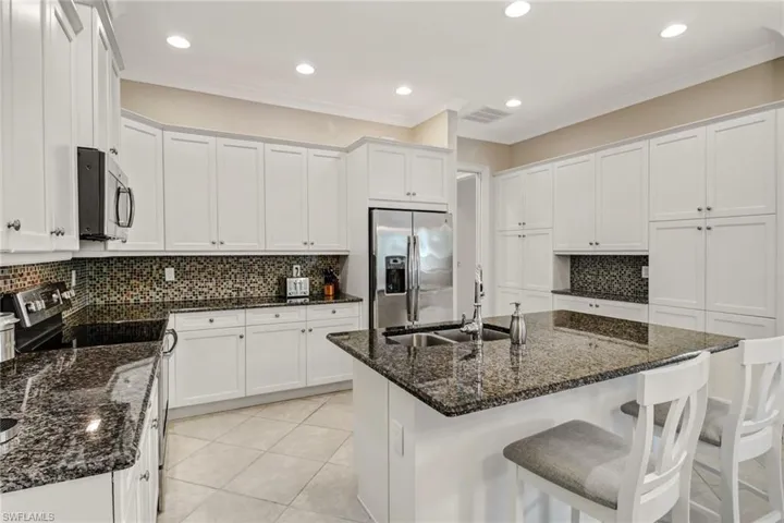 Kitchen featuring dark stone counters, a center island with sink, white cabinetry, and stainless steel appliances