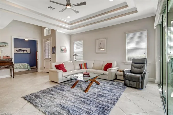 Living room featuring ceiling fan, a raised ceiling, light tile patterned floors, and a healthy amount of sunlight