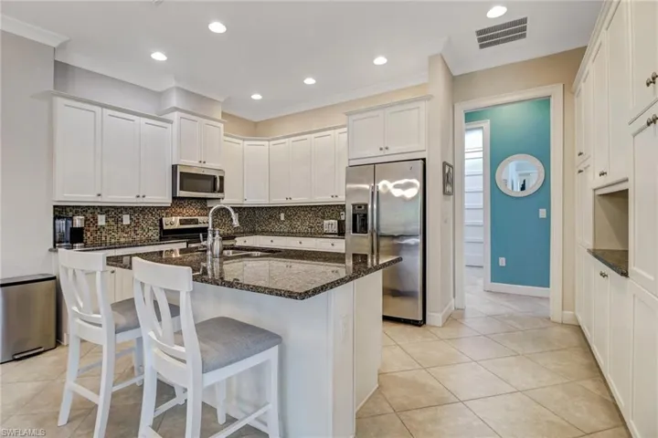 Kitchen with appliances with stainless steel finishes, dark stone countertops, white cabinetry, ornamental molding, and sink
