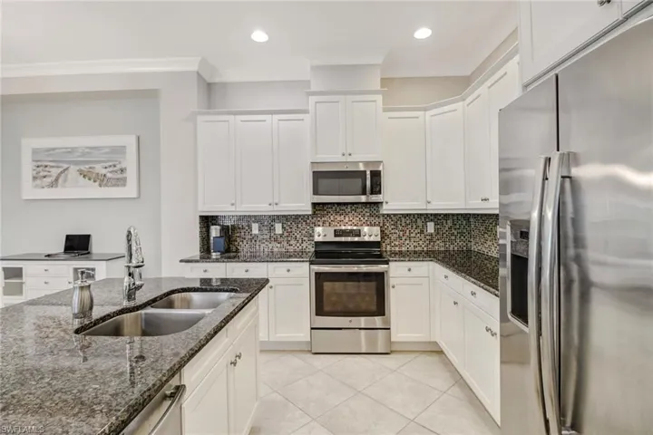 Kitchen with sink, white cabinetry, stainless steel appliances, dark stone counters, and crown molding