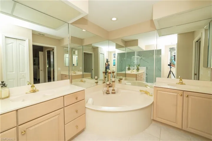 Bathroom featuring a marble finish shower, two vanities, light tile patterned floors, a bath, and a closet