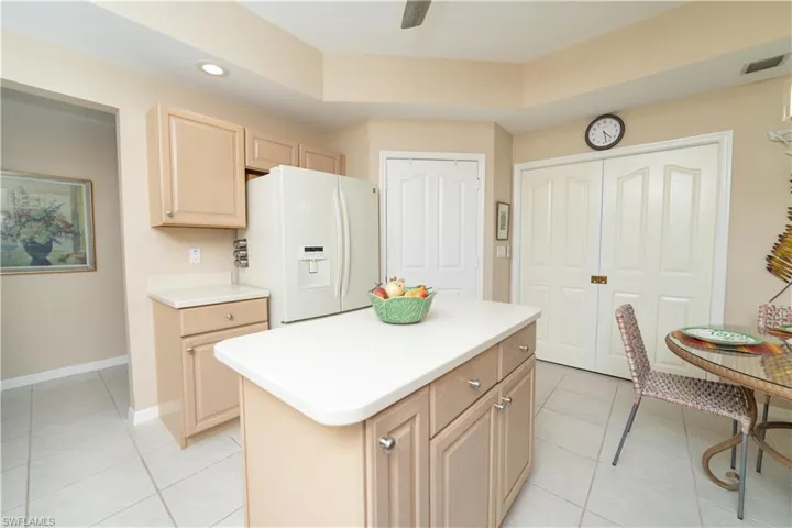 Kitchen with light tile patterned flooring, white fridge with ice dispenser, light countertops, light brown cabinetry, and recessed lighting
