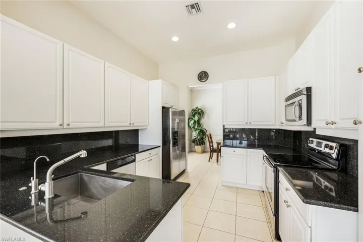 Kitchen with appliances with stainless steel finishes, white cabinetry, dark stone countertops, tasteful backsplash, and light tile patterned floors
