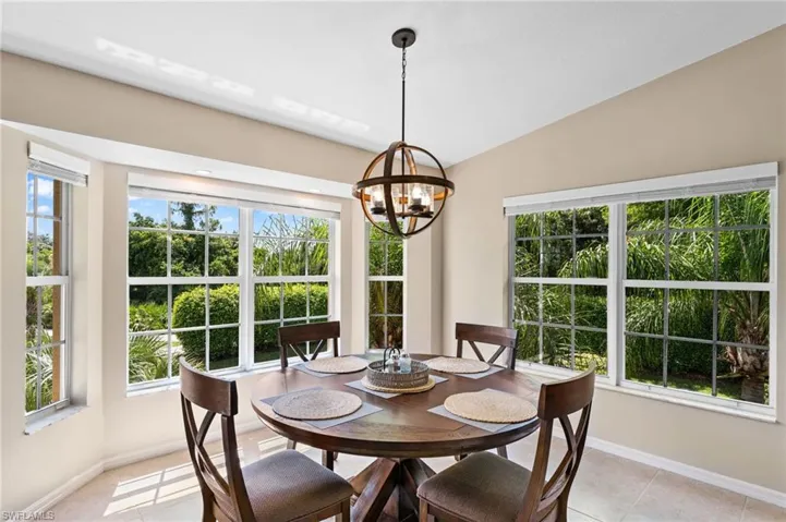 Tiled dining area featuring a notable chandelier, a healthy amount of sunlight, and lofted ceiling