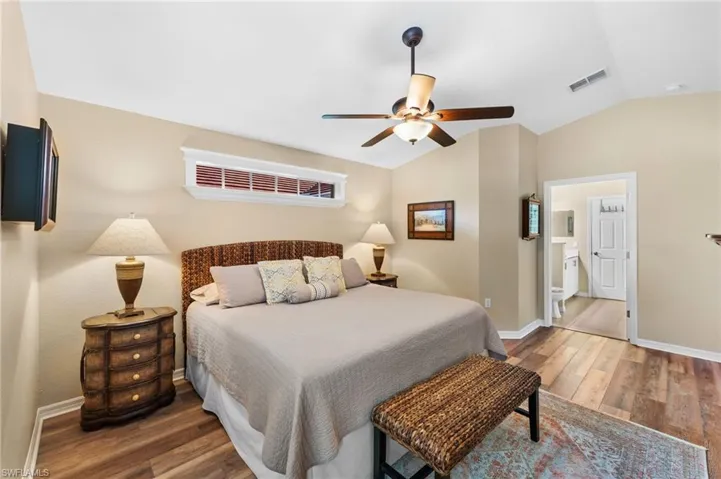 Bedroom with ensuite bath, hardwood / wood-style flooring, vaulted ceiling, and ceiling fan