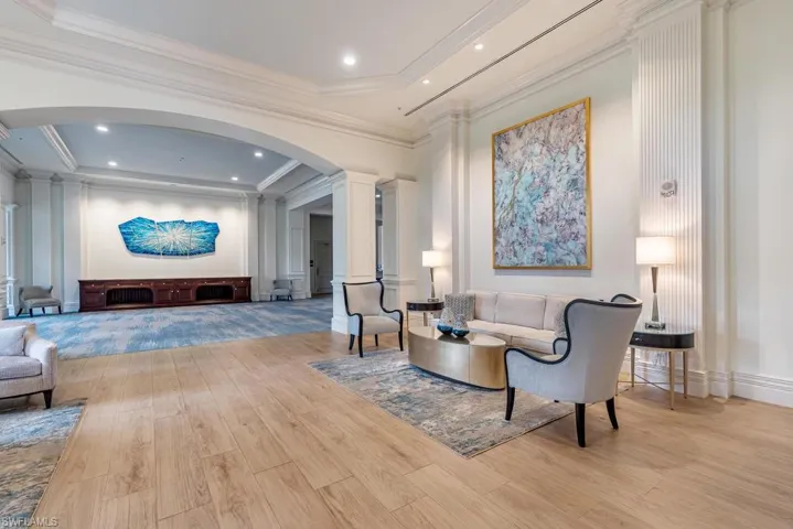 Living room featuring decorative columns, a tray ceiling, ornamental molding, and light hardwood / wood-style floors