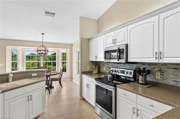 Kitchen featuring stainless steel appliances, sink, backsplash, decorative light fixtures, and light tile patterned floors
