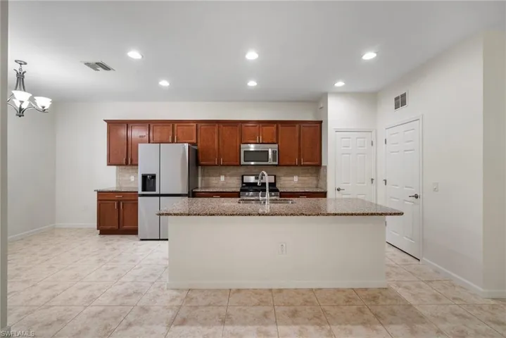 Kitchen featuring decorative backsplash, dark stone countertops, light tile patterned floors, an island with sink, and stainless steel appliances