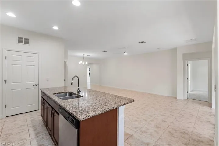 Kitchen featuring light tile patterned floors, dishwasher, a center island with sink, sink, and light stone counters