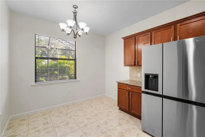 Kitchen with decorative backsplash, a chandelier, stainless steel fridge with ice dispenser, light stone countertops, and light tile patterned floors