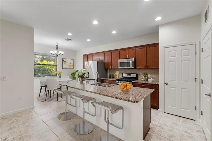Kitchen with decorative backsplash, a kitchen bar, a kitchen island with sink, light tile patterned flooring, and stainless steel appliances