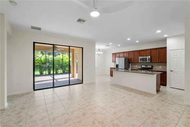Kitchen with a center island with sink, ceiling fan with notable chandelier, light tile patterned flooring, appliances with stainless steel finishes, and backsplash