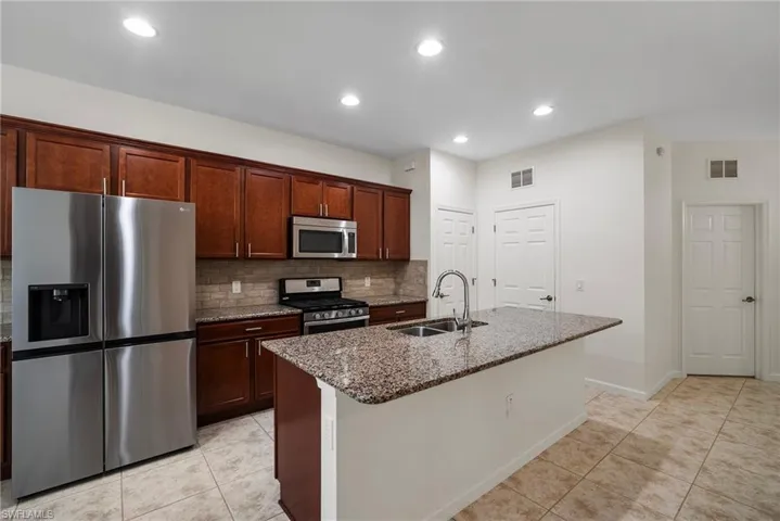 Kitchen with decorative backsplash, appliances with stainless steel finishes, sink, and an island with sink