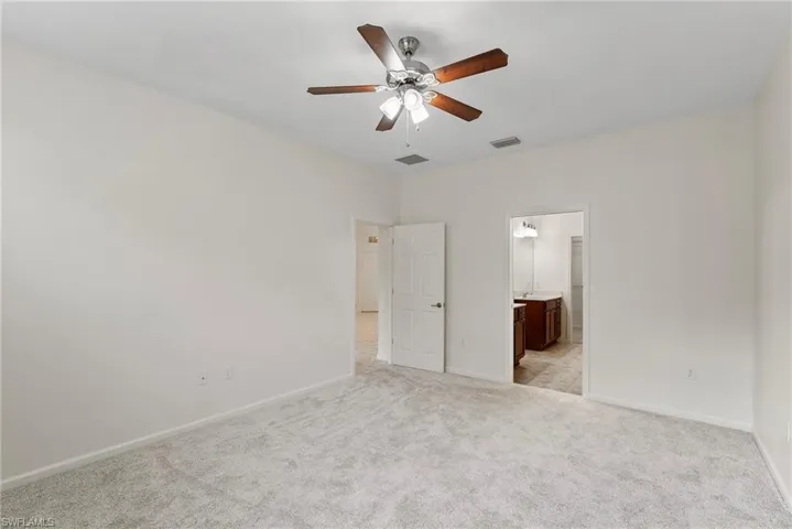 Unfurnished bedroom featuring ensuite bath, light colored carpet, and ceiling fan