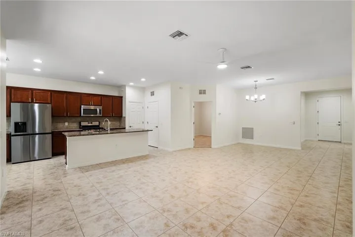 Kitchen featuring decorative backsplash, ceiling fan with notable chandelier, appliances with stainless steel finishes, a center island with sink, and light tile patterned floors