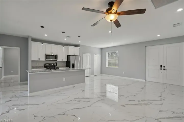 Kitchen with a kitchen island with sink, appliances with stainless steel finishes, ceiling fan, light tile patterned flooring, and decorative light fixtures