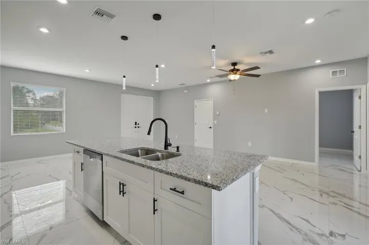 Kitchen featuring dishwasher, a center island with sink, ceiling fan, sink, and light stone counters