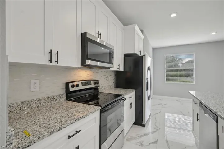 Kitchen with appliances with stainless steel finishes, light tile patterned flooring, backsplash, and light stone counters