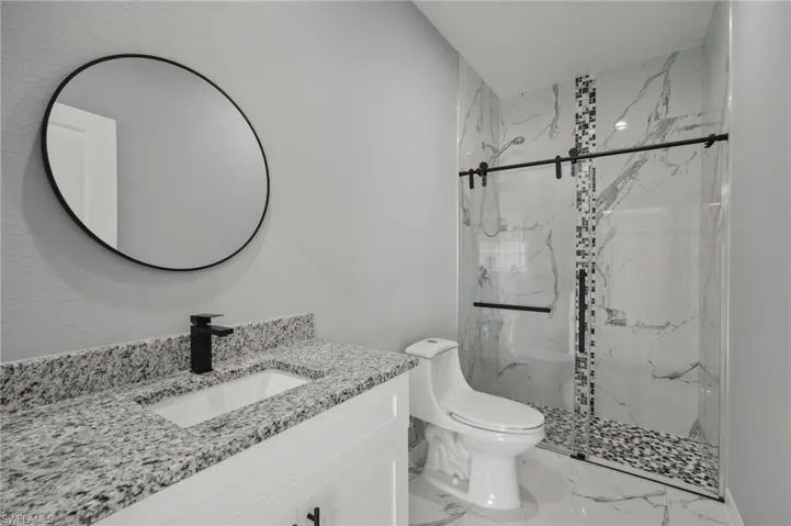 Bathroom featuring a shower with door, toilet, vanity, and tile patterned flooring